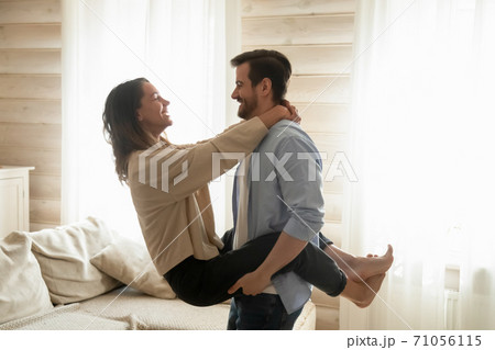 Affectionate boyfriend holds smiling girlfriend in arms lifting in air Affectionate boyfriend holds smiling girlfriend in arms lifting in air 71056115