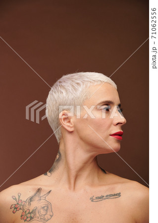 Manlike blond woman tattoos on neck and chest keeping head turned aside Manlike blond woman tattoos on neck and chest keeping head turned aside 71062556