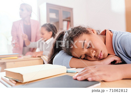 Exhausted girl keeping her head on desk on background of classmate and teacher 71062812