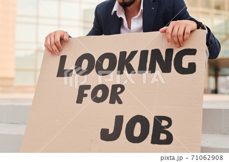 Hands of jobless man holding piece of cardboard with notice of looking for job Hands of jobless man holding piece of cardboard with notice of looking for job 71062908