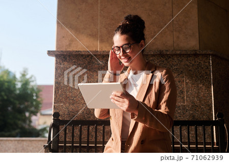 Young cheerful female broker in smart casualwear looking through online data 71062939
