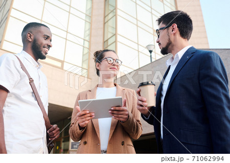 Three young intercultural colleagues in smart casualwear brainstorming outdoors Three young intercultural colleagues in smart casualwear brainstorming outdoors 71062994