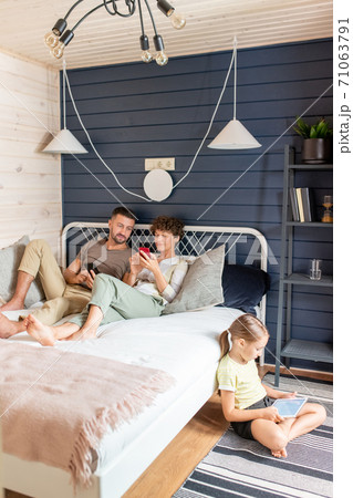 Little girl in casualwear using tablet while sitting on the floor by her parents 71063791