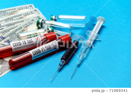 Close up 100 US dollar bills, vaccine ampoules and blood sample in test tube over blue background 71069341