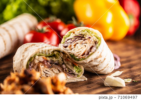 Kebab filled tortilla wraps on a table with vegetables in teh background 71069497