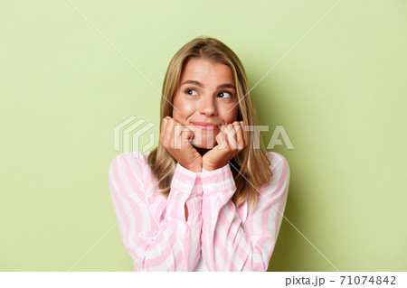 Close-up of beautiful blond girl dreaming about something, leaning on hands and smiling, looking left, standing over green background 71074842