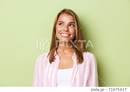Close-up of pretty blond girl in pink shirt, looking at upper left corner logo and smiling, standing over green background 71075817