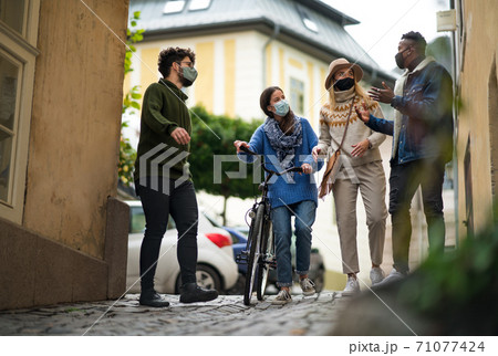 Group of young people with bicycle outdoors in town, walking. Coronavirus concept. 71077424