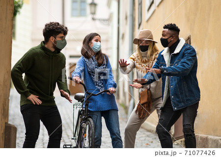 Group of young people with bicycle outdoors in town, talking. Coronavirus concept. Group of young people with bicycle outdoors in town, talking. Coronavirus concept. 71077426