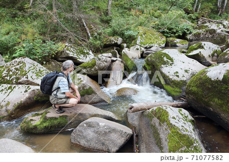 Man sitting on a stone near a mountain river Man sitting on a stone near a mountain river 71077582