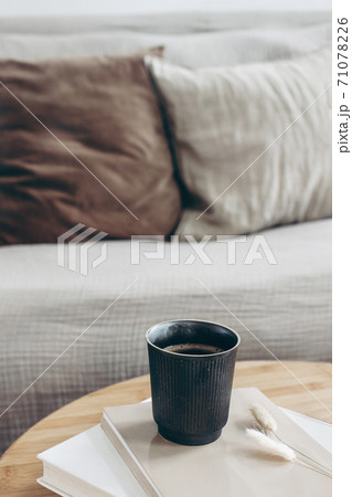 Books, dry bunny tail grass and black cup of coffee on round wooden table. Blurred beige sofa background with linen cushions. Hygge, cozy lifestyle concept. Scandinavian interior. Vertical. 71078226