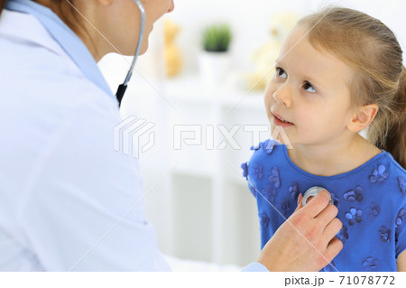 Doctor examining a little girl by stethoscope. Happy smiling child patient at usual medical inspection. Medicine and healthcare concepts 71078772