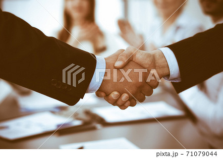 Business people shaking hands at meeting while theirs colleagues clapping and applauding. Group of unknown businessmen and women in modern white office. Success teamwork, partnership and handshake 71079044