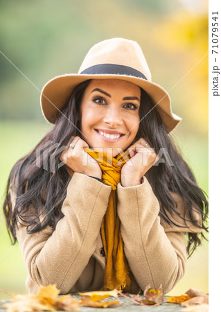 Cute young woman smilesat the camera dressed in beige jacket and hat and a yellow scarf on a cold autumn day 71079541