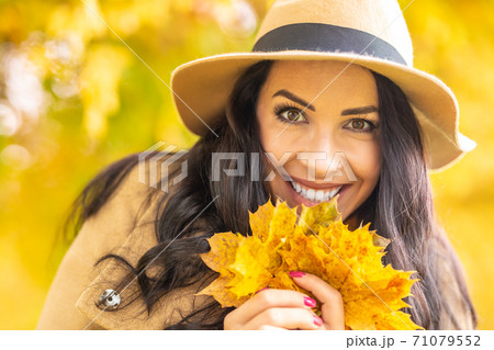 Pretty female smiles surrounded by yellow nature and holding fallen leaves 71079552