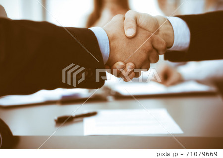 Business people shaking hands at meeting while theirs colleagues clapping and applauding. Group of unknown businessmen and women in modern white office. Success teamwork, partnership and handshake 71079669