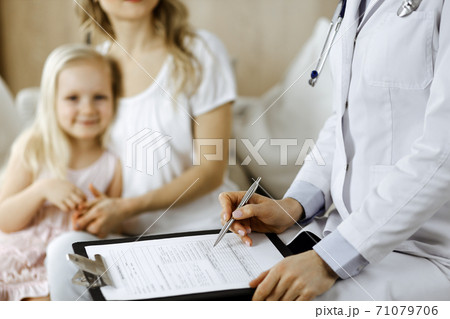 Doctor and patient. Pediatrician using clipboard while examining little girl with her mother at home. Happy cute caucasian child at medical exam. Medicine concept Doctor and patient. Pediatrician using clipboard while examining little girl with her mother at home. Happy cute caucasian child at medical exam. Medicine concept 71079706