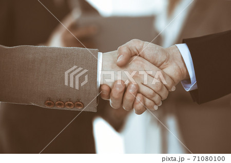 Business people shaking hands while standing with colleagues after meeting or negotiation, close-up. Group of unknown businessmen and women in modern office. Teamwork, partnership and handshake Business people shaking hands while standing with colleagues after meeting or negotiation, close-up. Group of unknown businessmen and women in modern office. Teamwork, partnership and handshake 71080100