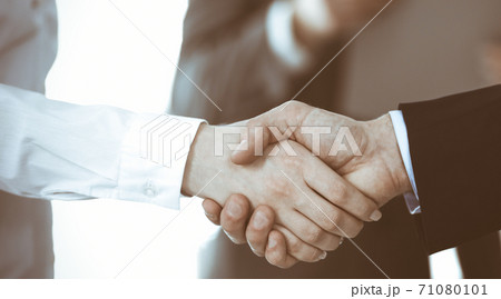 Business people shaking hands while standing with colleagues after meeting or negotiation, close-up. Group of unknown businessmen and women in modern office. Teamwork, partnership and handshake Business people shaking hands while standing with colleagues after meeting or negotiation, close-up. Group of unknown businessmen and women in modern office. Teamwork, partnership and handshake 71080101