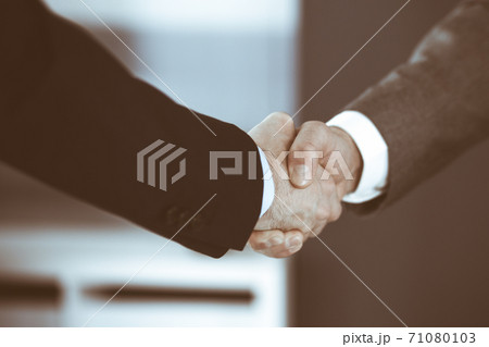 Business people shaking hands while standing with colleagues after meeting or negotiation, close-up. Group of unknown businessmen and women in modern office. Teamwork, partnership and handshake 71080103