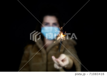Happy new year, portrait of a young woman wearing medical mask and holding sparklers light in the dark for Covid-19, Coronavirus and New year concept 71083416