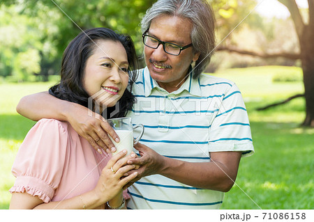 Senior couple embracing with holding glass of fresh milk in their hand on the park together. Senior couple embracing with holding glass of fresh milk in their hand on the park together. 71086158