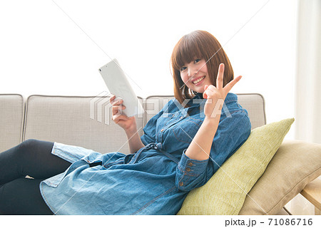 お家時間をソファでくつろぎながらタブレットを使って過ごす若い女性 71086716