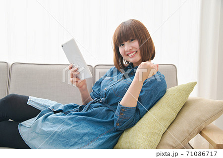お家時間をソファでくつろぎながらタブレットを使って過ごす若い女性 71086717
