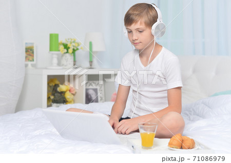 Boy listening to music on bed while having breakfast 71086979