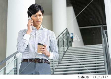 オフィスのロビーで飲み物を飲みながらスマホで会話をする若い男性 オフィスのロビーで飲み物を飲みながらスマホで会話をする若い男性 71089147