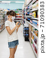 Young woman with face mask using mobile phone and buying groceries in the supermarket 71090383