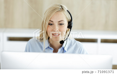 Blonde business woman sitting and communicated by headset in call center office. Concept of telesales business or home office occupation Blonde business woman sitting and communicated by headset in call center office. Concept of telesales business or home office occupation 71091371