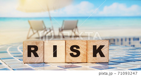 RISK word made with building blocks on relaxed beach background. Sun umbrella and sea. Business investment concept RISK word made with building blocks on relaxed beach background. Sun umbrella and sea. Business investment concept 71093247