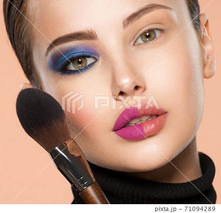 Portrait of a girl with cosmetic brush near face. Woman making makeup on the face using makeup brush. One half face of a beautiful white woman with bright makeup and the other is natural. Portrait of a girl with cosmetic brush near face. Woman making makeup on the face using makeup brush. One half face of a beautiful white woman with bright makeup and the other is natural. 71094289