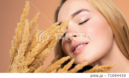 Calm Blonde girl with a bunch spring dry field flowers near the face - over colored background. Beauty face care concept. Calm Blonde girl with a bunch spring dry field flowers near the face - over colored background. Beauty face care concept. 71094439