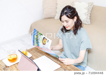 パンフを見ながらパソコンで旅行計画を立てる若い女性 71094446