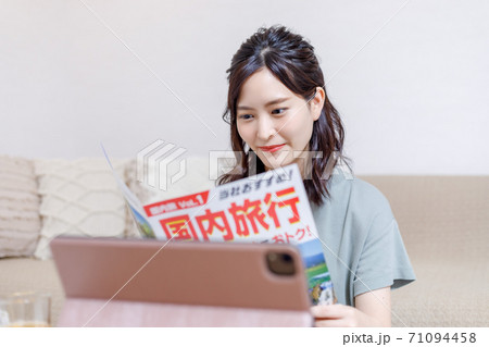 パンフを見ながらパソコンで旅行計画を立てる若い女性 71094458