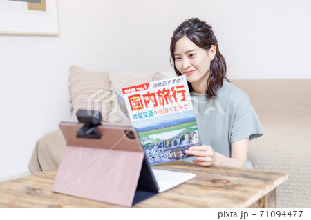 パンフを見ながらパソコンで旅行計画を立てる若い女性 71094477