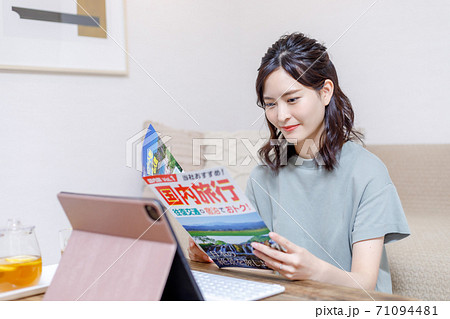 パンフを見ながらパソコンで旅行計画を立てる若い女性 71094481