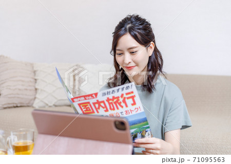 パンフを見ながらパソコンで旅行計画を立てる若い女性 71095563