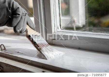 Painting old wooden window with white color. Brush in hand with grey glove 71095677
