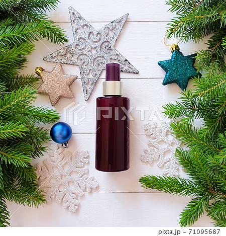 Top view of dark brown spray bottle mockup, fir branches, stars, balls on a white wooden table. Blank label bottle for branding. Natural organic spa cosmetics concept. Close-up, Christmas flatlay. 71095687