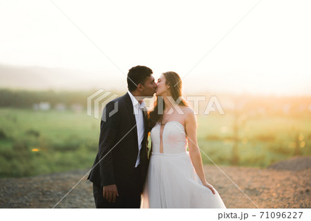 Beautiful bride and groom embracing and kissing on their wedding day outdoors Beautiful bride and groom embracing and kissing on their wedding day outdoors 71096227