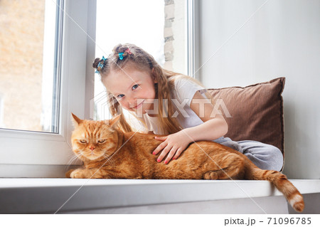 Cute child embraces with tenderness and love a red cat on window Cute child embraces with tenderness and love a red cat on window 71096785