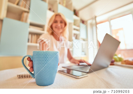 Blue cup on kitchen table in front of working woman 71099203