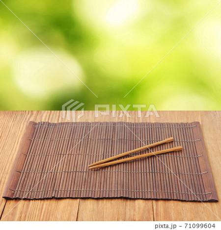 Sushi sticks on brown bamboo food placemat on wooden table against defocused green background. 71099604