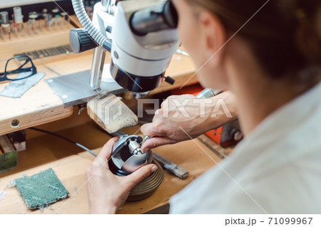 Diligent jeweler working on microscope at her workbench 71099967