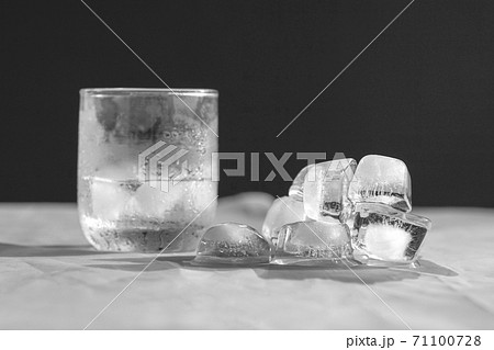 Half glass of water with ice cubes, and melting ice cubes on top of table 71100728