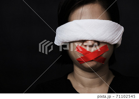 woman blindfold wrapping mouth with red adhesive tape, tied with chains and closed her eyes 71102545