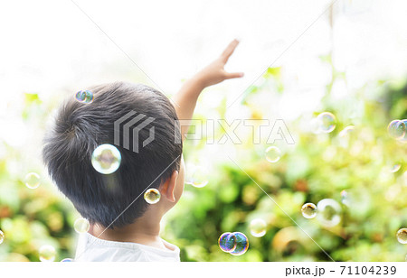 外でシャボン玉を掴もうと手を空に伸ばしている子供　空に向かって手を伸ばす子供 71104239